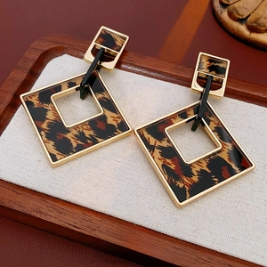 Elegant geometric leopard print drop earrings with gold square frames on a display mat
