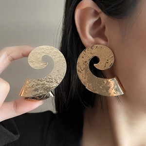 Close-up of oversized gold spiral earrings with a hammered texture on a model ear