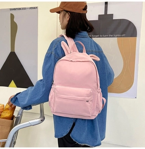 Rear view of a model wearing a pink rabbit ear backpack in a clean minimalist indoor setting