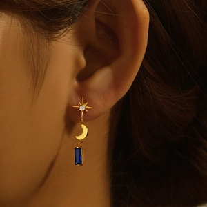 Detailed view of gold star and moon earrings with navy blue rectangular gemstones