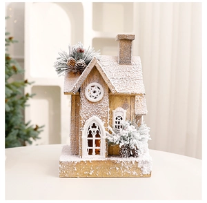 Close-up of wooden Christmas house with LED lights, artificial snow and pine cone details