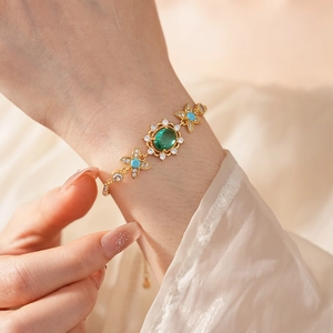 Gros plan d'un bracelet vintage doré avec une pierre verte et des détails floraux bleus