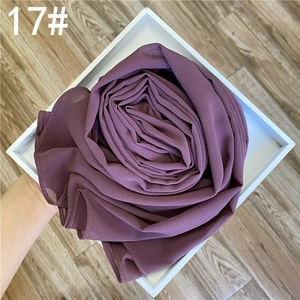 Détail d'une écharpe en mousseline violet foncé pliée dans une boîte cadeau
