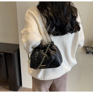 Close-up of black quilted bucket bag with gold chain strap on a model shoulder