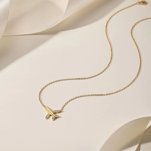 Detail of gold airplane pendant necklace with zircon wings on beige silk background