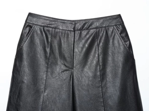 Detail of high-waist black faux leather pants showing pocket and pebbled texture