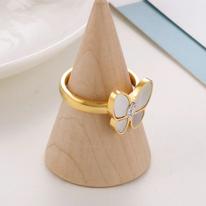 Detail eines goldenen Schmetterlingsrings mit weißen Muschelflügeln auf Holzständer