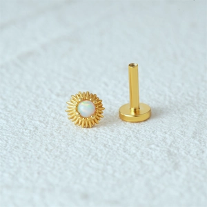 Detailed view of 16G gold sunburst piercing stud with central opal and flat back labret
