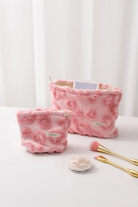 Détail de trousses à maquillage en peluche rose avec texture cœur et fermeture éclair