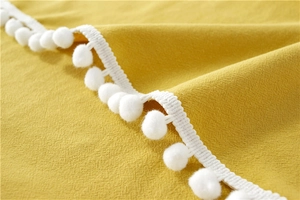 Macro detail of yellow washed cotton tablecloth showing weave texture and white pom-pom trim