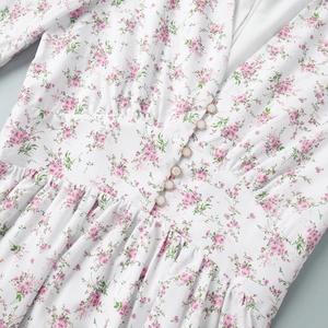 Detail of floral V-neck dress with pearl buttons and high-waisted pleats on white fabric