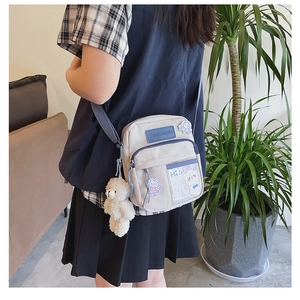 Petit sac bandoulière en toile grise avec zip bleu et pendentif ours porté par un mannequin
