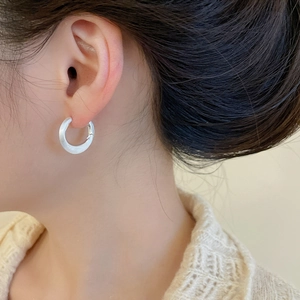 Macro view of C-shaped brushed silver earrings with pearl finish on model