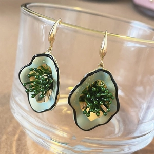 Detailed close-up of green floral earrings with gold hooks on a glass edge