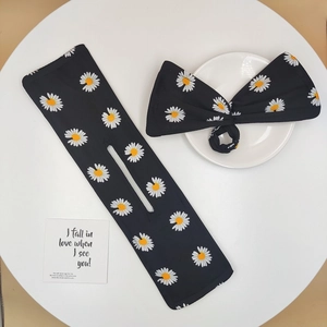 Flat lay of black floral daisy bun maker set with bow hair tie on a white table