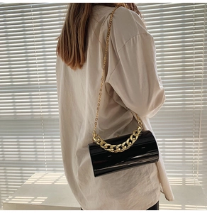 Detail shot of black mirror-finish cylinder bag with gold chain strap on a model