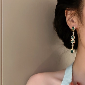 Primer plano de pendientes vintage de esmeralda con acabado dorado y cristales