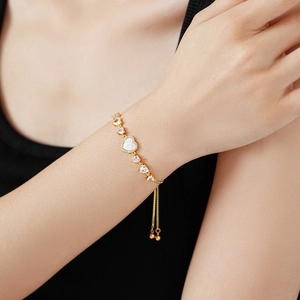 Detail of gold heart bracelet with mother of pearl and zircon on model's wrist
