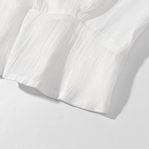 Close-up of white textured fabric showing fine stitching and pleated details on the skirt