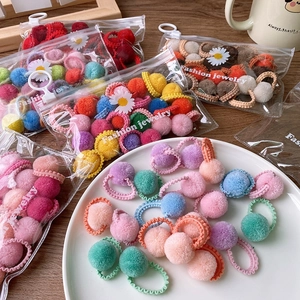 Detail of colorful plush pom-pom hair ties in a transparent daisy zipper storage bag