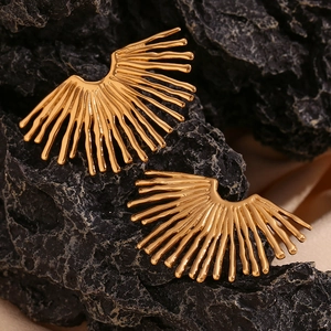 Macro view of 18K gold plated radial fan-shaped earrings on a black textured rock
