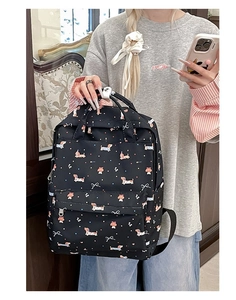 Detail of black graffiti backpack featuring dachshund and white bow prints with front pocket