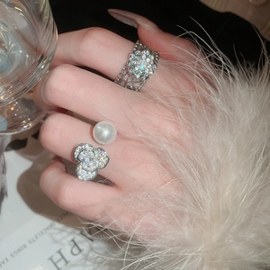 Détail d'une bague fleur en perle argentée et d'une bague en treillis avec zircons brillants