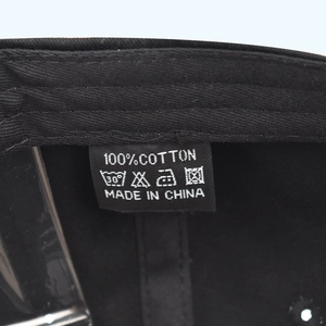 Detailed macro view of the 100% cotton care label and washing instructions on a black hat