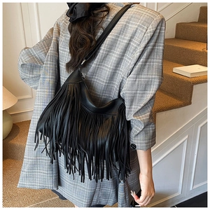 Detail of black leather shoulder bag with long fringes shown on a plaid blazer