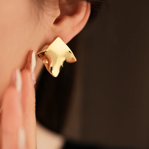 Gros plan détaillé de boucles d'oreilles carrées ondulées plaquées or avec fini poli brillant