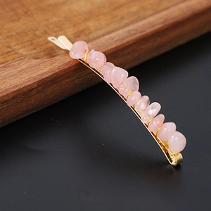Close-up of a gold hair clip with natural raw pink crystal stones on a dark tray