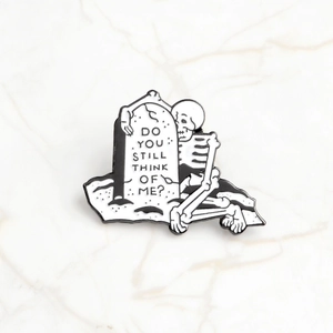 Detail of skull leaning on tombstone enamel pin with 'Do you still think of me' text