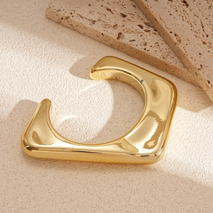 Macro detail of geometric gold cuff bracelet on a beige textured stone background