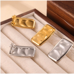 Macro view of gold and silver rectangular earrings with wavy texture in a jewelry box