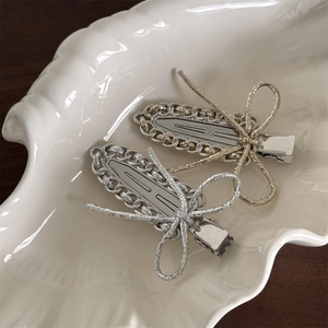 Close-up of gold and silver metal bow hair clips on a white ceramic shell tray