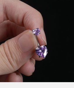 Close-up of silver belly ring featuring two purple heart-shaped stones on black background