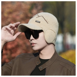 Close-up of beige knit earflap hat showing thick wool texture and logo patch