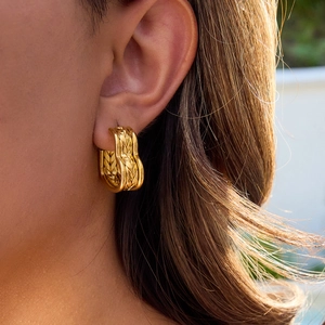 Close-up of gold stainless steel hoop earrings with woven texture worn by a model