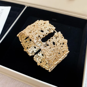 Détail du bracelet manchette doré avec des motifs floraux ajourés de style dentelle