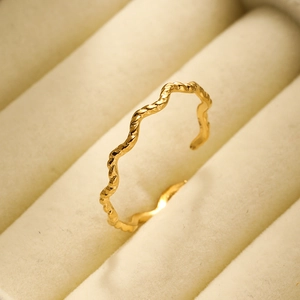 Macro shot of 18K gold plated wavy open ring resting on a beige velvet jewelry box