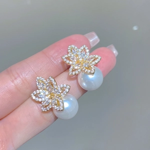 Detailed close-up of a floral pearl earring with sparkling zircons and a golden finish