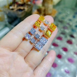 Elegant gold-plated earrings with square zirconia stones held by hand for size reference