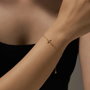 Detailed close-up of a gold s925 silver cross bracelet with zircon on a model's wrist