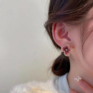 Elegant red crystal flower stud earrings with golden petals on female model's ear