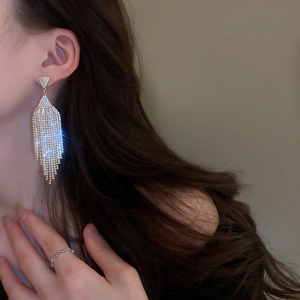 Close-up of model wearing silver long tassel earrings with sparkling heart-shaped zircons