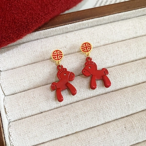 Detailed close-up of red pony pendant earrings with gold hollow stud in a jewelry box