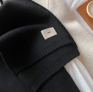 Close-up of black knitted scarf with fine stitching and a minimalist emo woven label