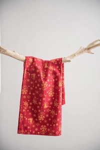 Vue détaillée du tissu de Noël rouge avec motifs dorés drapé sur une branche en bois