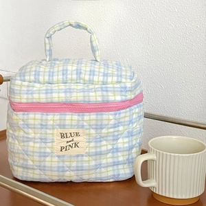 Detailed shot of teal quilted makeup bag with pink zipper on rustic wooden surface