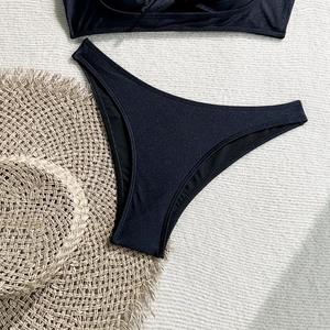 Flat lay of black bikini bottoms on a woven beach mat with a straw hat and soft shadows